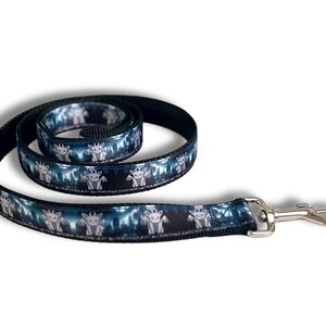 May include: A coiled pet leash featuring a repeating pattern of small, grey, winged dragon-like creatures against a dark blue and black background. The leash is constructed with black webbing and includes a silver-toned metal swivel snap hook.