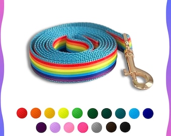 May include: A rolled-up, light blue dog leash with a rainbow stripe design. The leash has a gold-colored metal clasp. The rainbow stripes include red, orange, yellow, green, and purple. The leash is made of a durable, woven material.