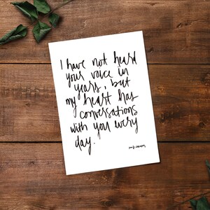 May include: A white card with black handwritten text that reads "I have not heard your voice in years, but my heart has conversations with you every day." The text is in a cursive font and the signature "your name" is at the bottom right corner of the card.