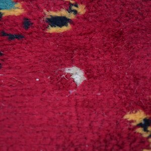 May include: Close-up of a red rug with a small hole in the centre. The rug has a pattern of yellow and black shapes.