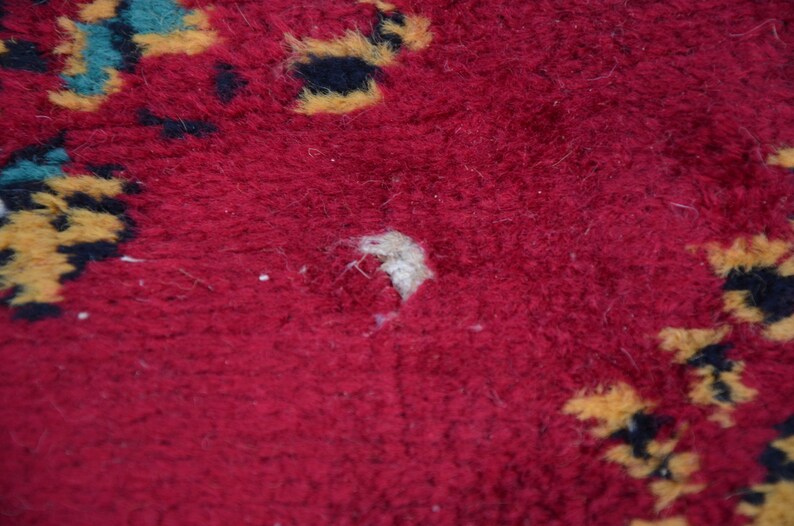 May include: Close-up of a red rug with a small hole in the centre. The rug has a pattern of yellow and black shapes.