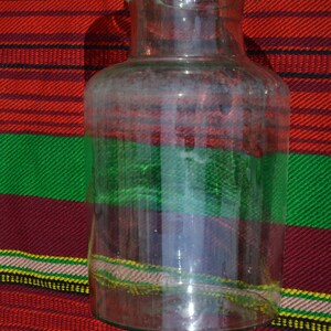 May include: A clear glass jar with a wide base and a narrow neck. The jar is set against a colorful background of red, green, and yellow stripes. The jar is empty and appears to be clean.