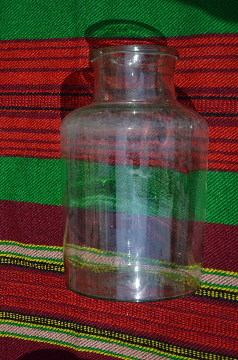 May include: A clear glass jar with a wide base and a narrow neck. The jar is set against a colorful background of red, green, and yellow stripes. The jar is empty and appears to be clean.