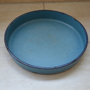 Peut inclure: Une poêle ronde en émail bleu clair avec un bord bleu foncé. La poêle a une texture mouchetée et repose sur une surface carrelée de couleur claire. Cette poêle de style vintage est adaptée à la cuisson et au service.