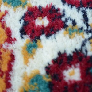 May include: Close-up of a white, fluffy rug with a colourful floral pattern. The rug features red, yellow, green, and blue flowers.