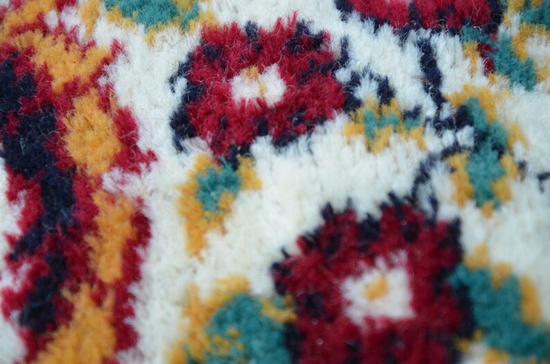 May include: Close-up of a white, fluffy rug with a colourful floral pattern. The rug features red, yellow, green, and blue flowers.