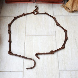 Peut inclure: Un support de plante en fer forgé rustique avec un crochet et une chaîne. Le support en métal marron est posé sur une surface carrelée, mettant en valeur sa forme et sa construction uniques. Idéal pour suspendre des plantes.