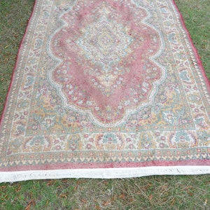 May include: A vintage rug with a pink, green and cream floral pattern. The rug has a white fringe border.