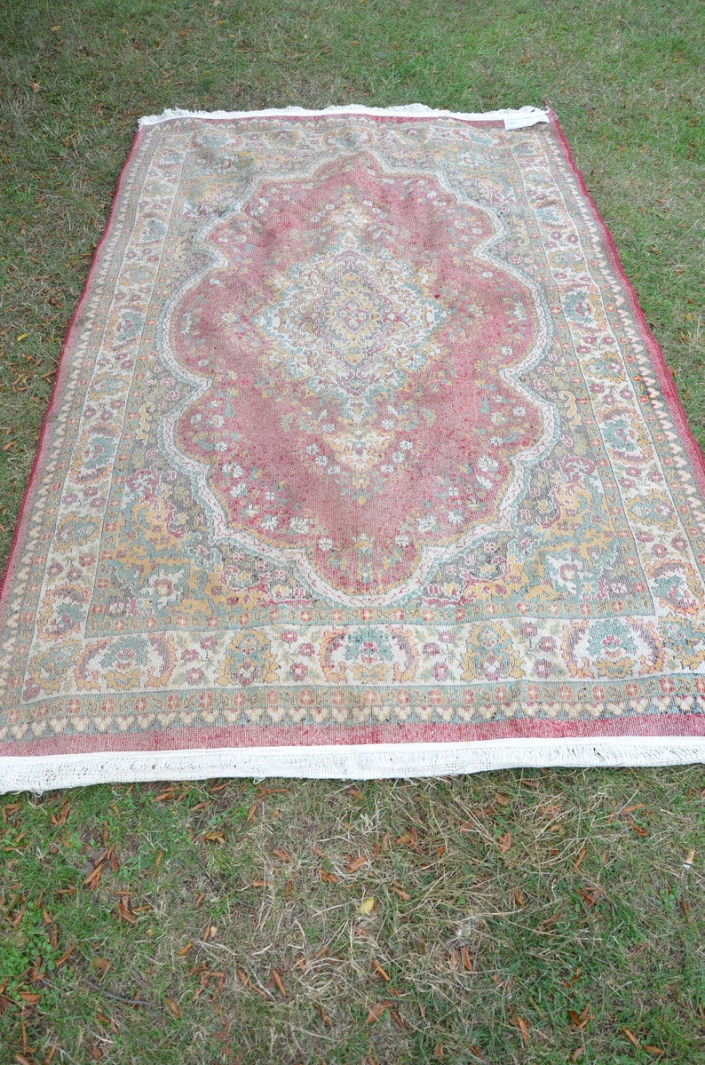 May include: A vintage rug with a pink, green and cream floral pattern. The rug has a white fringe border.