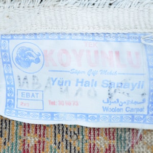 May include: A white tag with blue and pink text that reads "KOYUNLU Spor &Ccedil;ift Mekik Y&uuml;n Halı Sanayii EBAT 2x3 Tel: 30 96 73 السجادة من الصرف Woolen Carpet". The tag features a blue and white image of a ram's head.