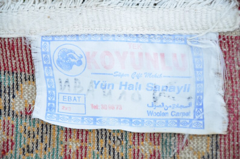 May include: A white tag with blue and pink text that reads "KOYUNLU Spor &Ccedil;ift Mekik Y&uuml;n Halı Sanayii EBAT 2x3 Tel: 30 96 73 السجادة من الصرف Woolen Carpet". The tag features a blue and white image of a ram's head.