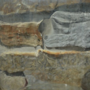 May include: A close-up of a cylindrical object with a layered, stone-like appearance. The colors range from gray and brown to tan and white, with a glossy, reflective surface. The object appears to be made of natural materials.