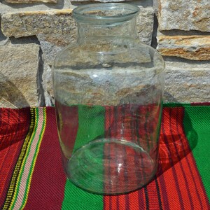 May include: A clear glass jar with a wide base and a narrow neck. The jar is sitting on a colorful striped textile with red, green, and yellow stripes. The background is a stone wall.