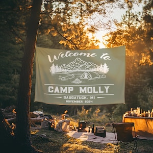 May include: A green welcome banner with white text that reads "Welcome to Camp Molly - Saugatuck, MI - November 2024". The banner features a white illustration of mountains, a lake, and a tent.
