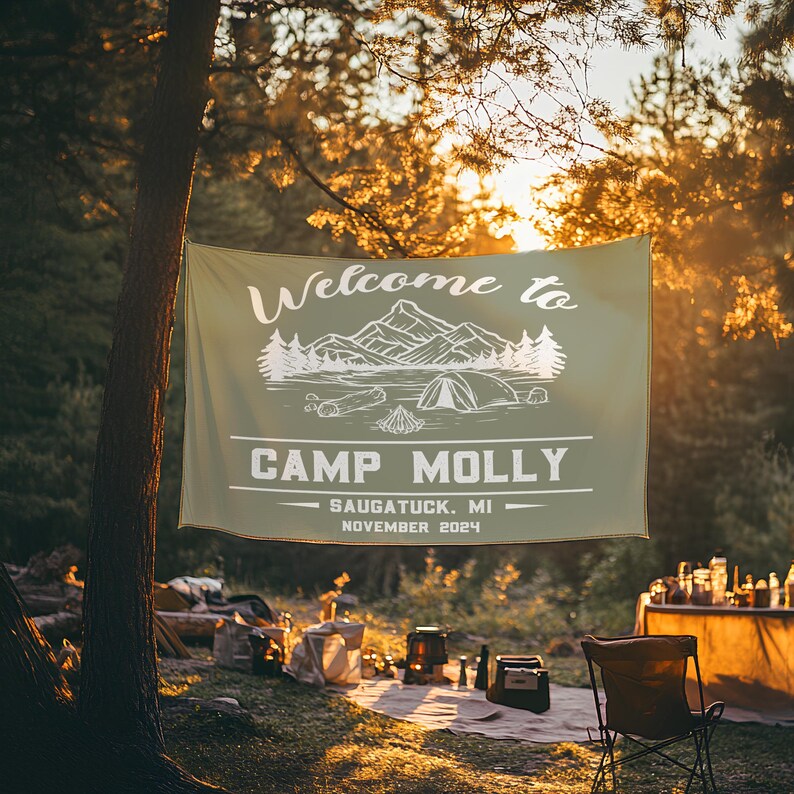 May include: A green welcome banner with white text that reads "Welcome to Camp Molly - Saugatuck, MI - November 2024". The banner features a white illustration of mountains, a lake, and a tent.