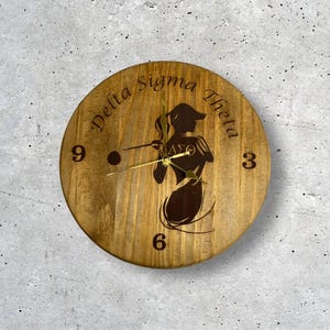 May include: A wooden clock with a silhouette of a woman playing golf. The clock face has the text "Delta Sigma Theta" and the numbers 3, 6, and 9.