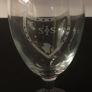 May include: A clear glass wine glass with an etched design of a shield with the letters "SPS" and the number "19" inside.
