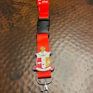 May include: Red lanyard with white text "1911" and a silver fraternity crest. The lanyard has a black clip and a silver swivel hook.