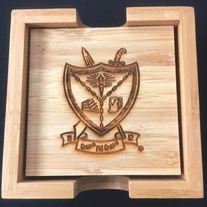 May include: A wooden coaster with an engraved design featuring a shield with a torch, books, a cup, and swords. The shield is surrounded by a chain and the text "1904 Phi Gamma Delta 1904" is below the shield.