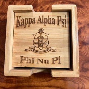 Könnte beinhalten: Ein Untersetzer-Set aus Holz mit einem lasergravierten Design mit den griechischen Buchstaben Kappa Alpha Psi und Phi Nu Pi. Das Untersetzer-Set ist aus natürlichem Bambus gefertigt und hat eine hellbraune Farbe.