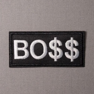 May include: A rectangular black embroidered patch featuring the white text BO$$ in a bold, sans-serif font. The letters are stitched with a visible thread texture, and the dollar signs replace the letter S, creating a distinct graphic design.