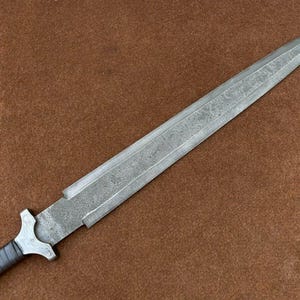 May include: A silver knife with a textured blade and a black handle. The knife has a sharp point and a straight edge.