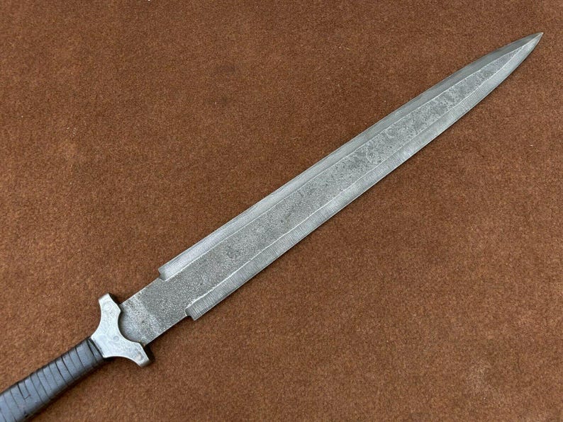 May include: A silver knife with a textured blade and a black handle. The knife has a sharp point and a straight edge.