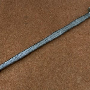 May include: A long, black-wrapped sword with a silver blade and a triangular handle. The sword is lying on a brown surface.