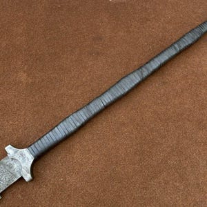 May include: A long, silver-colored sword with a black leather handle. The blade is textured and the handle is wrapped in leather.