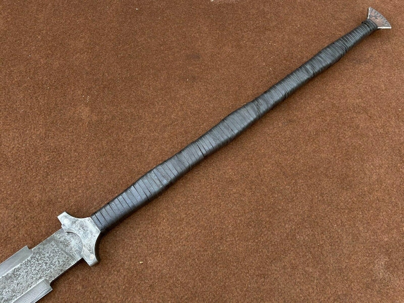 May include: A long, silver-colored sword with a black leather handle. The blade is textured and the handle is wrapped in leather.