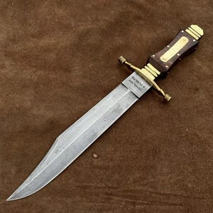 May include: A silver-colored Bowie knife with a wooden handle and brass accents. The handle has a brass inlay with the text "ROBERT E. LEE" and "MASTER CUTLER".