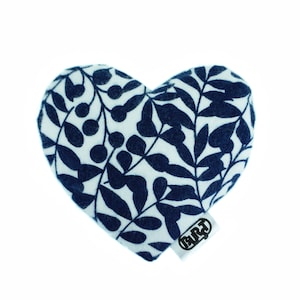 Könnte beinhalten: Ein weißes herzförmiges Kissen mit einem blauen Blumenmuster. Das Kissen hat ein kleines schwarzes Etikett mit dem Text "BART" darauf.