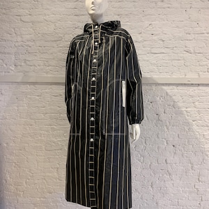May include: A black, long, hooded coat with vertical cream-colored stripes. The coat has a button-up front, a zipper pocket, and a drawstring hood. The coat is displayed on a mannequin.