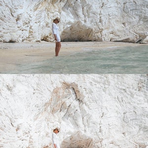 K&ouml;nnte beinhalten: Eine Frau in einem wei&szlig;en Kleid steht an einem wei&szlig;en Sandstrand vor einer wei&szlig;en Klippe. Das Wasser hat eine hellblaue Farbe.