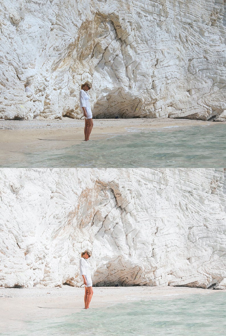 K&ouml;nnte beinhalten: Eine Frau in einem wei&szlig;en Kleid steht an einem wei&szlig;en Sandstrand vor einer wei&szlig;en Klippe. Das Wasser hat eine hellblaue Farbe.
