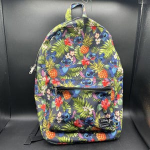 May include: A dark blue backpack featuring an all-over print of the character Stitch from Lilo and Stitch, surrounded by green tropical palm leaves, yellow pineapples, and red hibiscus flowers. It includes a front zippered pocket and a Disney label.
