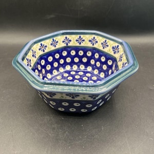 May include: An octagonal ceramic bowl featuring a deep blue interior decorated with white polka dots. The rim displays a pattern of small blue flowers on a light green background, while the exterior base is adorned with white polka dots on blue.