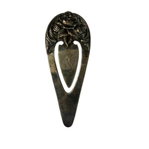 May include: A silver-toned metal bookmark with a teardrop shape and a pointed bottom. The top section features an embossed floral design with roses and leaves, while the center contains a cutout space with a smooth, triangular metal insert.