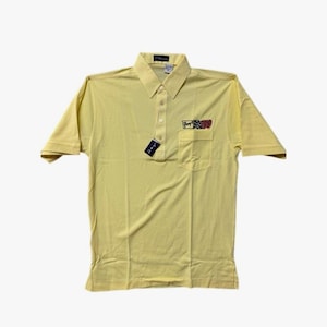 May include: A yellow short-sleeved polo shirt with a small pocket on the left side. The pocket has a colorful graphic of a checkered flag and the text "Tommy Hilfiger" on it.