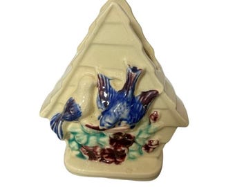 May include: A cream-coloured ceramic birdhouse figurine, featuring blue birds and burgundy flowers. The birdhouse has a triangular roof and a rectangular base. The birds are perched on green leaves. A decorative item.