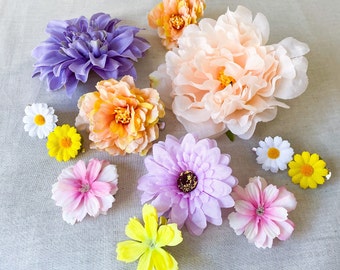 May include: A collection of colorful artificial flowers in various sizes and styles. The assortment includes large peony-like blooms in peach and smaller daisy-like flowers in white and yellow. Other flowers are lavender, pink, and orange.