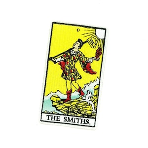 May include: Embroidered patch featuring a tarot card design. The card depicts a figure with a staff, a dog, and a sun, set against a yellow background. The text "THE SMITHS" is at the bottom of the card.
