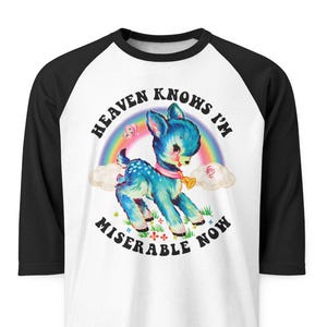 May include: White raglan shirt with black sleeves featuring a blue deer graphic with a rainbow and the text "Heaven Knows I'm Miserable Now". The graphic is a vintage-inspired design.