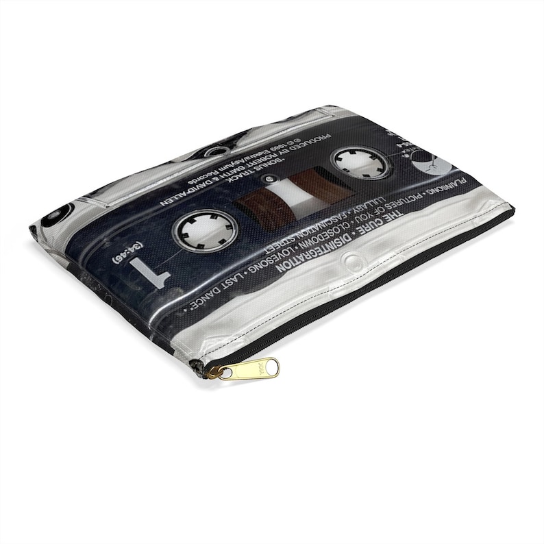 May include: A zippered pouch featuring a cassette tape design. The pouch is black, silver, and brown, with text including "The Cure Disintegration" and song titles. The zipper is gold-colored.