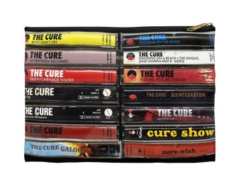 May include: Black zippered pouch featuring a collage of The Cure album cassette tapes. The design includes album titles like "Boys Don't Cry," "Seventeen Seconds," and "Kiss Me, Kiss Me, Kiss Me." The pouch has a gold-colored zipper.