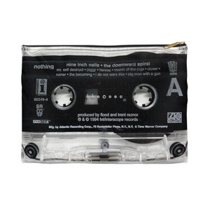 May include: A clear zippered pouch with a black cassette tape design. The tape features the text "nine inch nails the downward spiral" and song titles. The pouch has a gold-colored zipper and is made of a clear, transparent material.