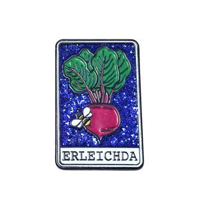 May include: A blue and white enamel pin with a red beet and a bee on a sparkly background. The text "ERLEICHDA" is printed on the pin.