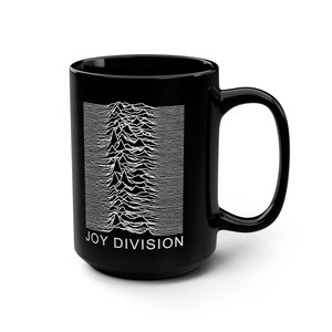 May include: A black ceramic mug featuring a white graphic print of the Joy Division Unknown Pleasures pulsar wave pattern on the front. The text JOY DIVISION is printed in white capital letters directly below the wave design on the mug.