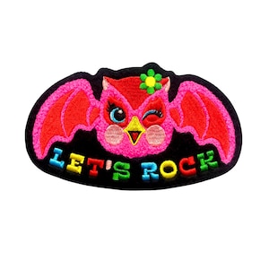 May include: Embroidered patch featuring a pink owl with red wings, winking and wearing a flower. The text "LET'S ROCK" is in colorful letters on a black background. This patch is perfect for adding to clothing or accessories.