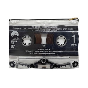 May include: A zippered pouch featuring a cassette tape design. The black and white graphic includes the album title "Disintegration" by The Cure, track names, and Elektra Records branding. The pouch has a gold zipper.